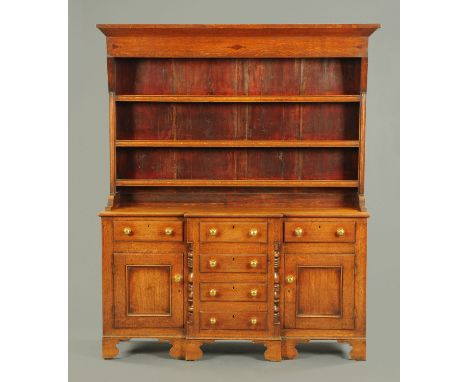 An early 19th century oak dresser with Delft rack, the base fitted with a series of drawers and cupboards with brass knob han