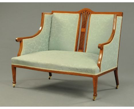 An Edwardian inlaid mahogany two seater settee, upholstered in green floral patterned material and raised on tapered legs of 