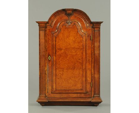 A Queen Anne walnut hanging cabinet, with arched moulded top above a fielded panelled door opening to shelves and flanked by 