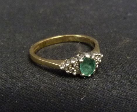 A 9ct. Gold Emerald and Diamond Dress Ring, set with a central emerald flanked by diamonds within a pierced setting