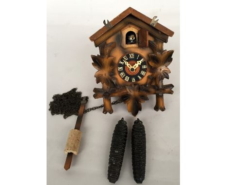 A Black Forest cuckoo clock with traditional wooden foliage design, white dial, Roman numerals and pine cone weight, 20.5cmH 