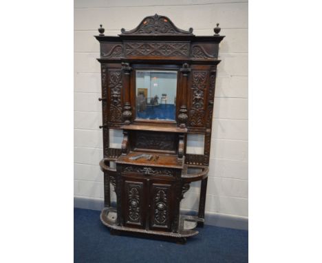 A 19TH CENTURY HEAVILY CARVED OAK HALL STAND, with a pediment and finials to top, a central bevel edged mirror flanked by Cor