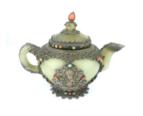 An antique Sino-Tibetan white metal mounted jade teapot, studded with cabouchon coral and other stones, to each side a Hindu 