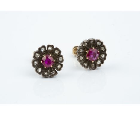 A PAIR OF RUBY AND DIAMOND CLUSTER EAR STUDS, each designed as a flowerhead cluster, centred with a cushion-shaped ruby borde