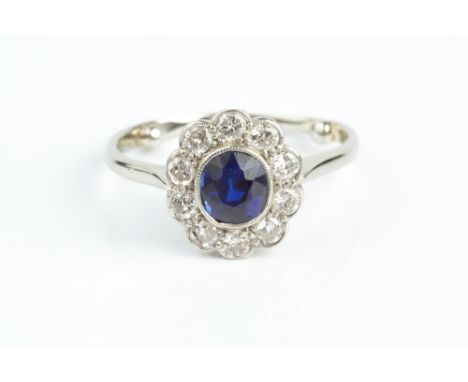 A SAPPHIRE AND DIAMOND CLUSTER RING, the cushion-shaped mixed-cut sapphire in millegrain collet setting, bordered by round br