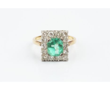 AN EMERALD AND DIAMOND CLUSTER RING, the octagonal step-cut emerald claw set within a border of round brilliant-cut diamonds,