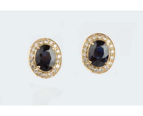 A PAIR OF SAPPHIRE AND DIAMOND CLUSTER EAR STUDS, each oval mixed-cut sapphire claw set within a border of round brilliant-cu