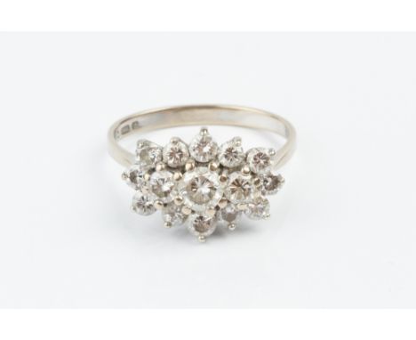 A DIAMOND CLUSTER RING, centred with a trio of round brilliant-cut diamonds, bordered by graduated further brilliants in claw