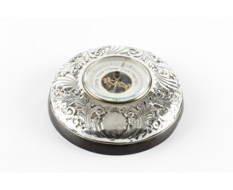 AN EDWARDIAN SILVER MOUNTED ANEROID BAROMETER, embossed with stylised scrolling foliage and having white enamel dial, by T.H.