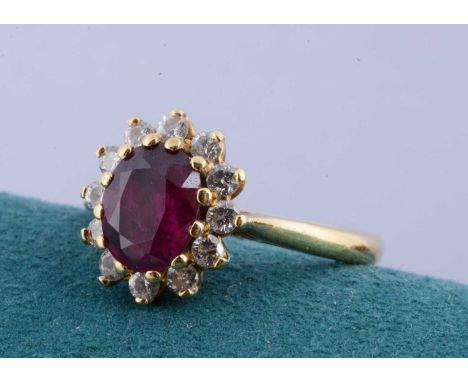 An 18ct gold ruby and diamond cluster ring, the mixed oval cut ruby in claw setting surrounded by twelve brilliant cut diamon