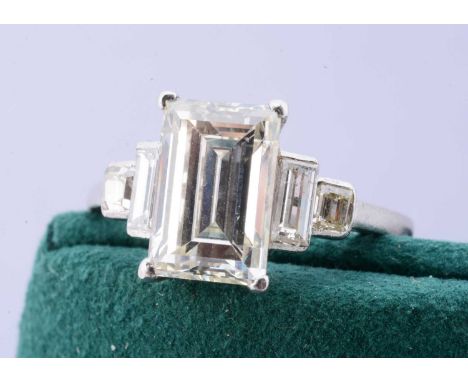 A diamond solitaire ring, the baguette central stone in claw setting flanked by two graduated baguette cut collet set diamond