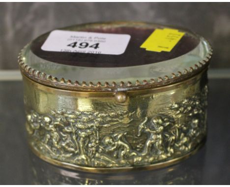 An attractive oval shaped brass cased trinket box with putti scenes and bevelled glass lid