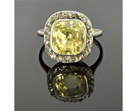 A yellow sapphire and diamond set cluster ring, mounted with the cushion shaped pale yellow sapphire at the centre, within a 