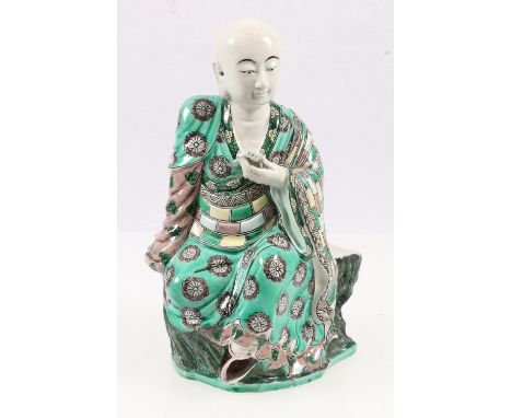 Early 20th century Chinese famille verte model of a monk in Buddhist robe seated on a tree trunk, 21cm CONDITION REPORT: Chip