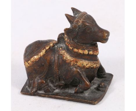19th century bronze model of a sacred bull, decorated with garlands, part gilded, on a low base, 7.5cm x 8cm.
