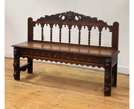 A late Victorian oak hall bench of 18th century design, the green man and acanthus carved pediment over an arcaded and bobbin