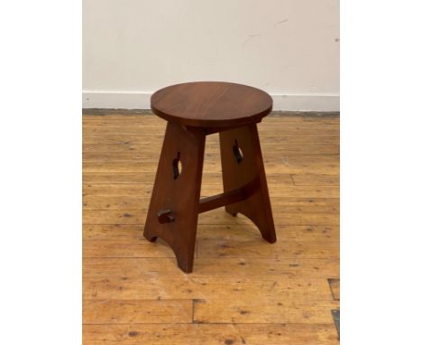 An Arts and Crafts period walnut lamp table, the circular top raised on pierce carved and splayed panel end supports united b