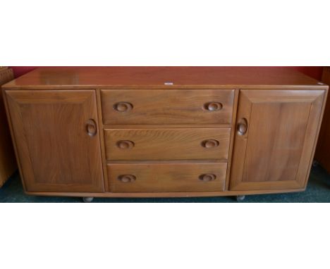 A light Ercol sideboard, centred by three long drawers flanked by a pair of cupboard doors, 155.5cm wide