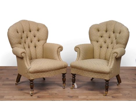 A pair of Victorian style button back armchairs, with scroll over arms above turned front legs terminating in brass castors, 