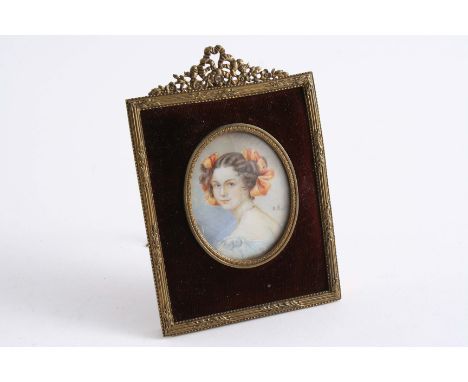 A SMALL OVAL MINIATURE PORTRAIT  of a girl with tied orange ribbons in her hair, brass & velvet covered easel frame;  4"  (10