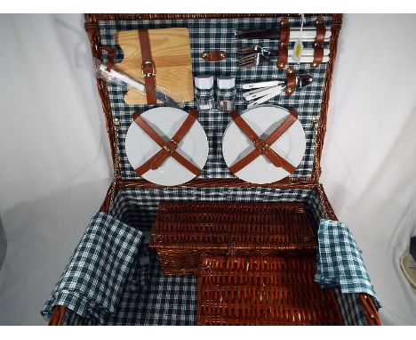 A good quality wicker picnic basket containing a 4 place setting to include ceramic plates, mugs, wine glasses, chopping boar