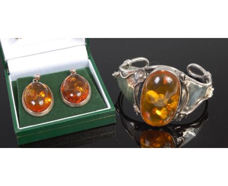 A sterling silver and clear orange amber set bangle; together with a pair of white metal and amber set ear studs (2) 