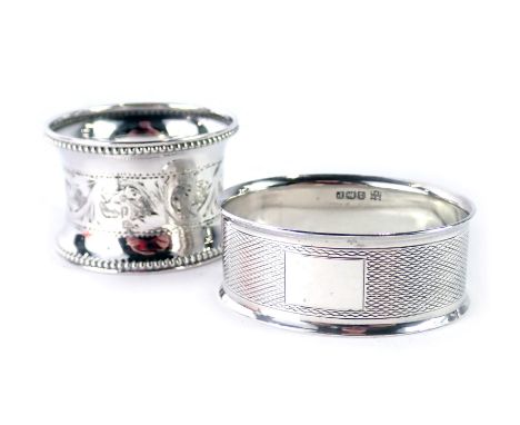 Two silver napkin rings, comprising an oval example with engine turned decoration and vacant shield, and another with central