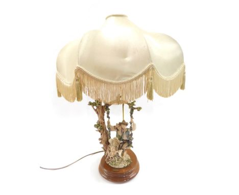 A Florence table lamp, of girl and boy on swing, with a gold shade, on wooden circular base, 72cm high. 