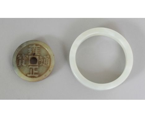 A CHINESE JADE BANGLE, 2.8in diameter, the inner rim 2.2in diameter; together with a piece of Chinese jade 'cash', 1.8in diam