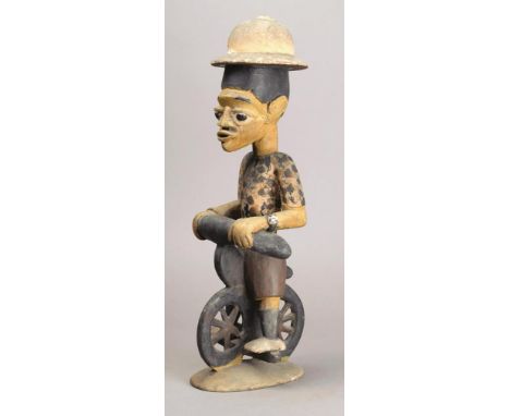 A Yoruba cyclist figure Nigeria wood and paint, the figure wearing a pith helmet, polka dot shirt, a watch and shorts, sittin