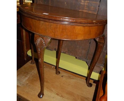 An early 20th century walnut and figured walnut demi-lune fold-over card table, having a baize lined interior, on shell cappe