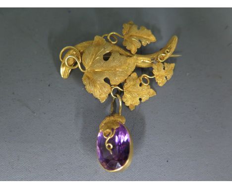 A yellow metal brooch in the form of vine leaves with an amethyst pendant hanging below tests as 9ct