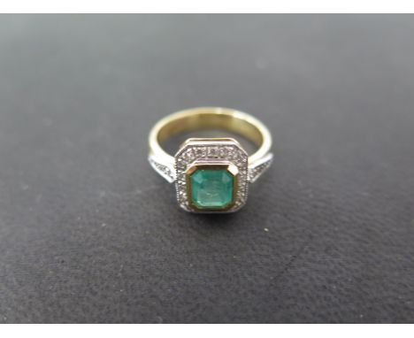 A pretty 18ct gold emerald and diamond ring - the central emerald of classic emerald cut form measures approx 8mm by 6mm and 