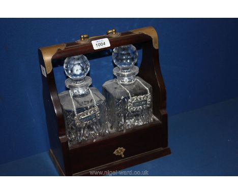 A wooden Tantalus with two non-matching cut glass decanters and three white metal labels for Whisky, Brandy and Sherry, with 