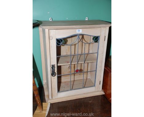 A small, limed Pine Wall Cabinet having moulded top over a single leaded glazed door with clear and stained panel, opening to