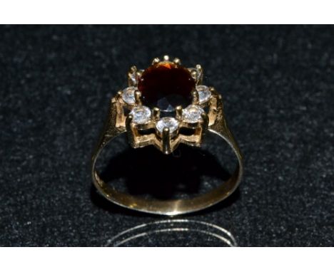 A red garnet and cubic zirconia floral cluster ring, central red oval garnet surround by a band of eight white cubic zirconia