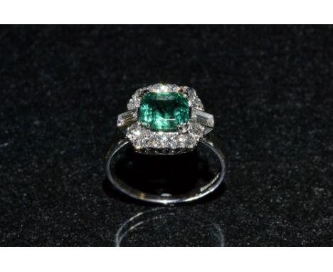 An emerald and diamond ring, central square cushion cut emerald, approx 1.5ct, surround by a band of twelve round brilliant a