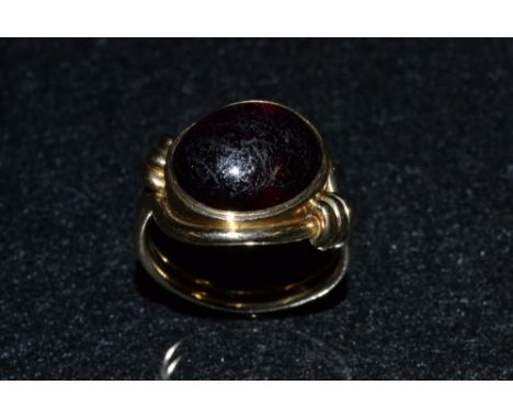 A gold coloured metal and garnet lady's ring, single oval red garnet cabochon, offset within a double layer scrolling surroun