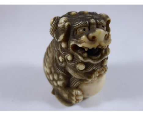 JAPANESE IVORY NETSUKE CARVED AS A DOG OF FO HOLDING A BALL WITH BALL TONGUE