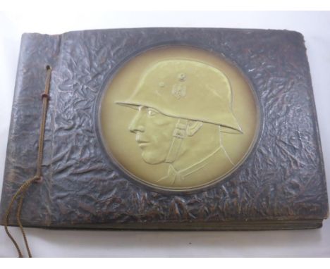 FASCINATING ALBUM OF WWII GERMAN MILITARY PHOTOGRAPHS MOUNTED IN AN ALBUM EMBOSSED WITH GERMAN HELMET DESIGN TO FRONT COVER