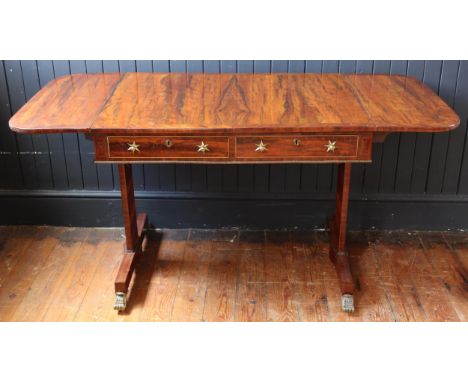 A Regency Rosewood and Crossbanded Drop Leaf Sofa Table with stretched hexagonal twin supports terminating in four gilt brass