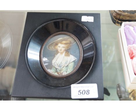 A black ebonised framed portrait miniature of a girl in a green hat.
