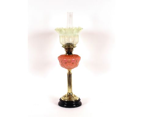 A brass column table oil lamp, having pink opaque glass foliate reservoir and tinted Vaseline glass shade, 72cm high overall