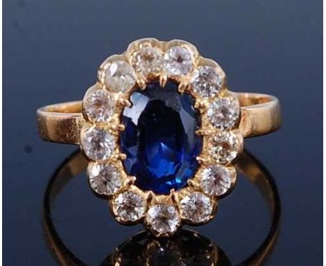 A yellow metal sapphire oval cluster ring, featuring an oval faceted sapphire claw set within a border of thirteen 2.6mm roun