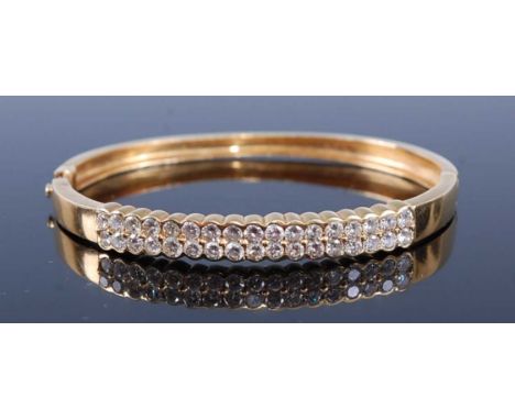 A yellow metal diamond set hinged bangle, arranged as two rows of seventeen round brilliant cut diamonds, each weighing appro