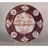 An 18th century Vauxhall delft plate with reserved panels of flowers and fence on a manganese