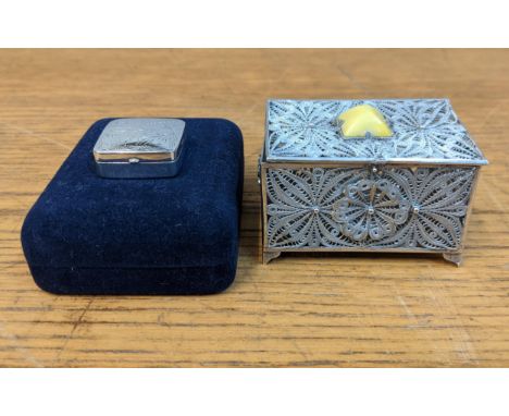 A silver filigree box decorated with floral emblems with a yellow pyramid shaped tablet on the lid and silver pill box, Londo