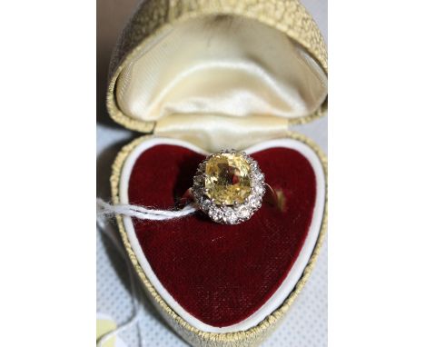 A yellow stone, (probably a sapphire) and fourteen stone diamond cluster ring. Centre stone 11mm high approx. In gold marked 