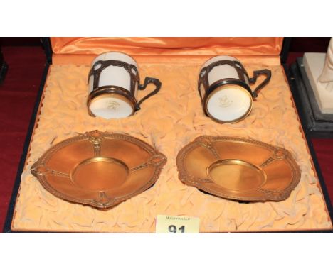 A pair of cased continental coffee cans with gilt metal holders and gilded metal saucers. (one coffee can repaired)