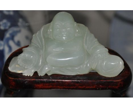 A Chinese jade figure of a Buddha, seated and raised on a wooden base, W. 12cm.